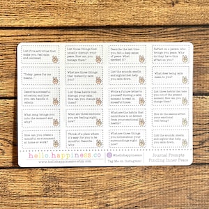 May include: A white sticker sheet with journal prompts for finding inner peace. The prompts are in small rectangular boxes with a peace sign icon. The sticker sheet has the website hello.happiness.co and the Instagram handle @hellohappinessco.