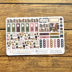 May include: A sticker sheet with a Hobo Weeks Kit design, featuring autumn-themed illustrations. The stickers include labels for each day of the week, along with decorative elements like books, coffee cups, and mushrooms. The text "hello.happiness.co" is visible.