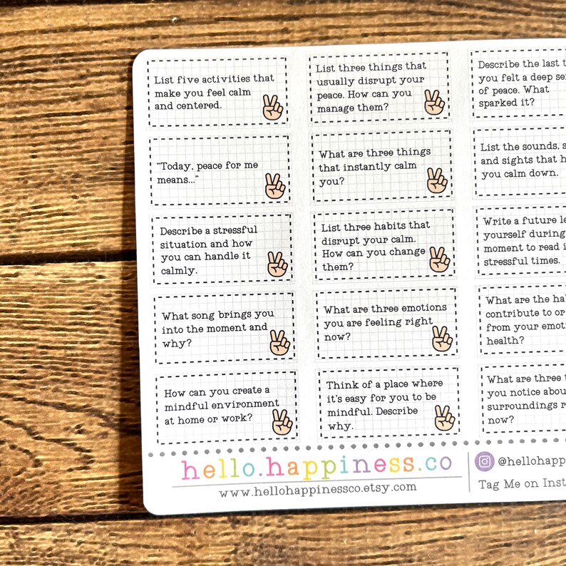 May include: A sheet of stickers with mindfulness prompts in black text on white rectangles. The stickers feature questions like "List five activities that make you feel calm" and include a hand with a peace sign. The website hello.happiness.co is visible.
