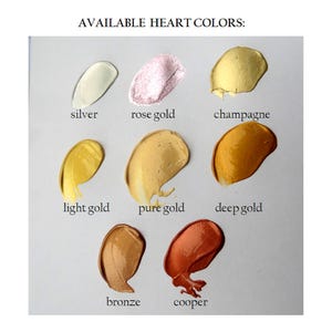 May include: A color chart titled AVAILABLE HEART COLORS displaying eight metallic paint swatches labeled silver, rose gold, champagne, light gold, pure gold, deep gold, bronze, and cooper. Each swatch shows a distinct metallic hue and texture.