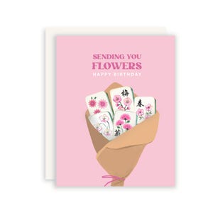 May include: A pink greeting card featuring a bouquet of mahjong tiles wrapped in brown paper. The tiles are decorated with pink floral illustrations and black Chinese characters. The text reads SENDING YOU FLOWERS HAPPY BIRTHDAY in pink and white.