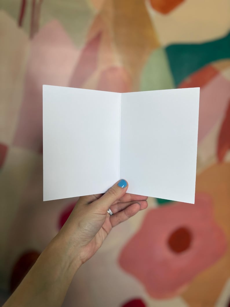 May include: A blank, rectangular, white greeting card held open to reveal two empty, smooth, matte-finish interior panels. The card is constructed from thick, high-quality paper stock, featuring a clean, sharp center fold and crisp, straight edges.