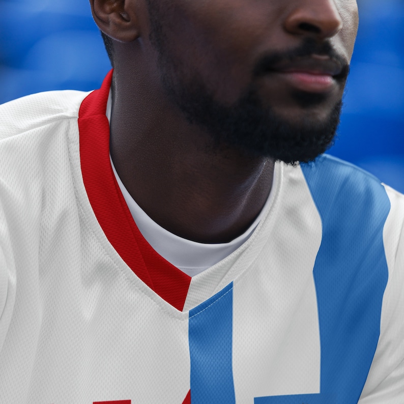 May include: A white jersey with red and blue trim. The jersey has a v-neck and is made of a breathable material.