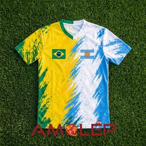 Puede incluir: Una camiseta de fútbol con cuello en V y diseño dividido. Un lado presenta los colores y la bandera de Brasil, el otro lado los colores y la bandera de Argentina. La camiseta tiene un cuello verde y el texto "AMOLEP" en la parte inferior.