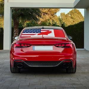 Könnte beinhalten: Ein rotes Auto mit einem Aufkleber auf der Heckscheibe, der die amerikanische und kanadische Flagge zeigt. Die Flaggen bestehen aus kleinen Quadraten, was einen pixeligen Effekt erzeugt.