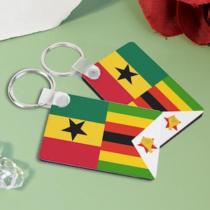 May include: Two silver keychains with rectangular tags featuring the flags of Ghana and Zimbabwe. The Ghanaian flag is red, yellow, green, and black with a black star in the center. The Zimbabwean flag is green, yellow, red, and black with a white triangle containing a yellow star and a bird.
