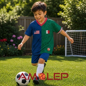 Puede incluir: Un joven con una camiseta de fútbol azul y verde con las banderas de Estados Unidos y México. La camiseta tiene un cuello rojo y ribetes blancos. La persona está pateando un balón de fútbol blanco y negro sobre un césped verde.