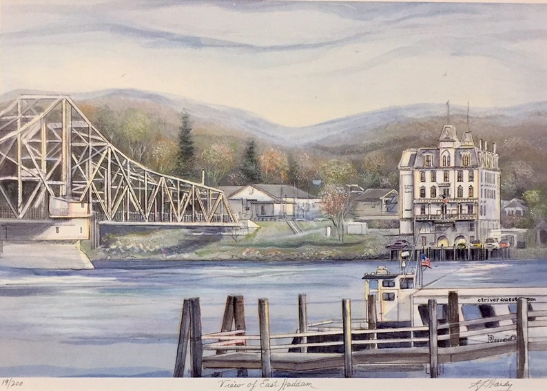 May include: A watercolor painting depicting a view of East Haddam, Connecticut. The painting features a wooden bridge over a river, a white building with a tower, a small boat docked at a pier, and a mountain range in the background.