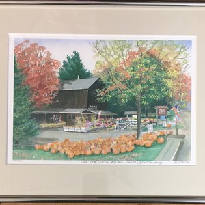 以下が含まれることがあります： 木造の建物と「The Old Cider Mill」と書かれた看板のある農場の売店の水彩画。建物の前にはカボチャが置かれ、木々には秋の紅葉が描かれている。