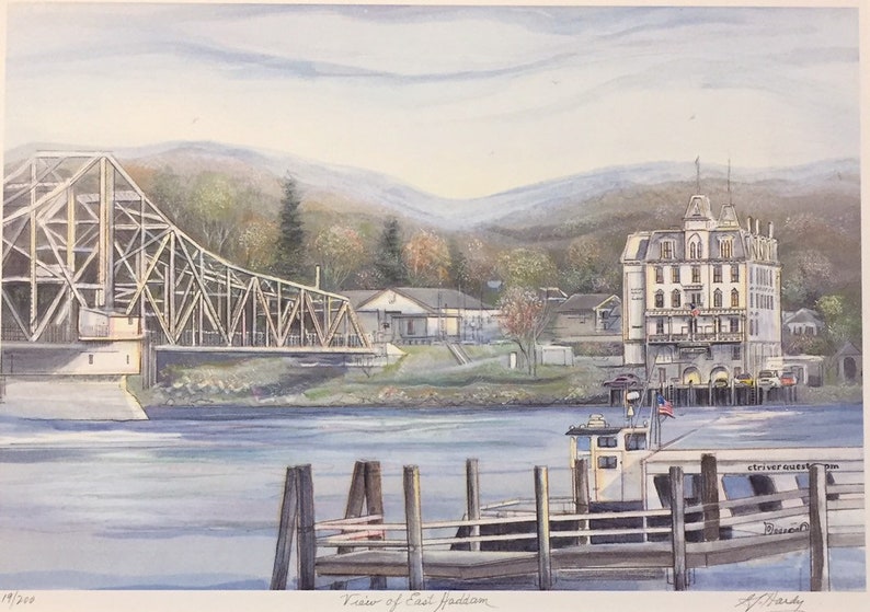 May include: A watercolor painting of a view of East Haddam, Connecticut. The painting features a wooden bridge, a white building with a tower, a boat docked at a pier, and a mountain range in the background.