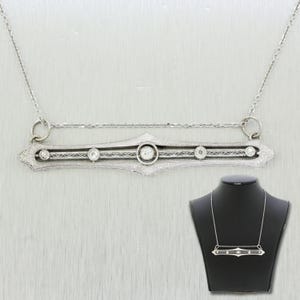 May include: A delicate silver necklace with a filigree bar pendant set with five round diamonds. The pendant is accented with intricate details and a delicate chain.