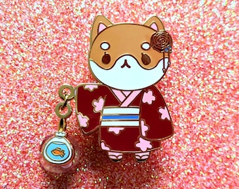 May include: A gold-tone enamel pin featuring a Shiba Inu dog wearing a red and pink kimono with a blue sash. The dog is holding a small glass orb with a goldfish inside. The pin has a rose and a dangling charm.