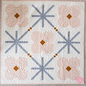 Quilt featuring alternating pink floral shapes and blue geometric stars on a cream background. Each floral shape has a brown diamond center.