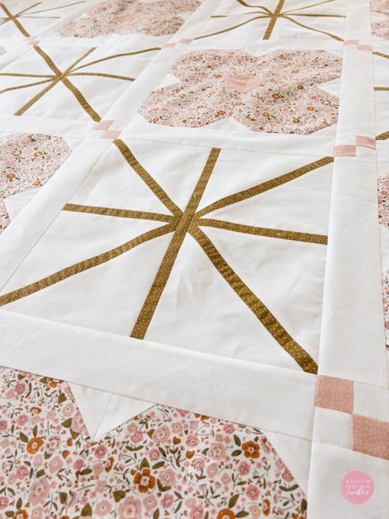 A quilt with star patterns in gold on white squares, framed by pink floral fabric. The quilt displays a harmonious, cozy, and crafted aesthetic.