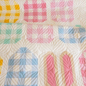 A quilt with pastel colors features geometric patterns, including squares, circles, and rectangles in pink, blue, yellow, and green tones, creating a cozy and cheerful ambiance.