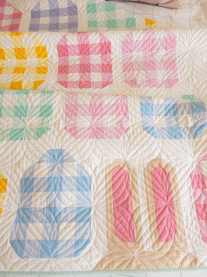 A quilt with pastel colors features geometric patterns, including squares, circles, and rectangles in pink, blue, yellow, and green tones, creating a cozy and cheerful ambiance.
