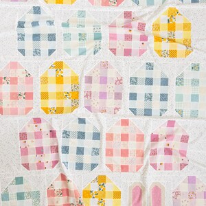 Colorful quilt with pastel checks in shades of pink, blue, yellow, and purple on a white speckled background. Cozy, homemade aesthetic.