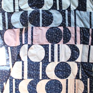 May include: A patchwork quilt with a repeating pattern of white, pink, and navy blue shapes. The design includes circles, half-circles, and vertical stripes. The navy blue fabric has a small white floral pattern.