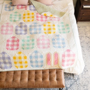 Colorful quilt with geometric patterns in pastel shades of yellow, pink, blue, and green on a bed. The mood is cozy and inviting.