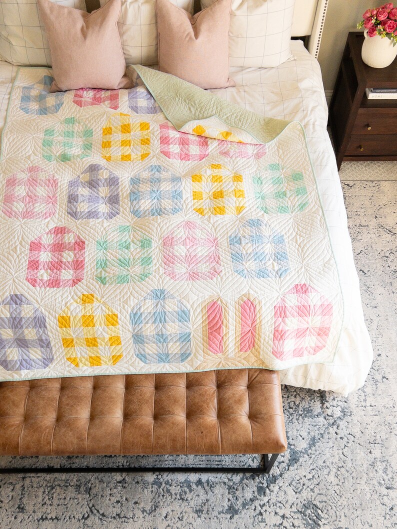 Colorful quilt with geometric patterns in pastel shades of yellow, pink, blue, and green on a bed. The mood is cozy and inviting.