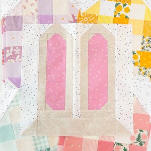 A colorful quilt block arrangement featuring pink and beige bunny ears at the center, surrounded by patchwork in pastel shades and floral patterns, creating a playful and cheerful tone.