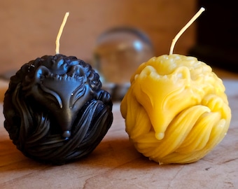 May include: Two small, round candles shaped like a curled up fox. One candle is black and the other is yellow.