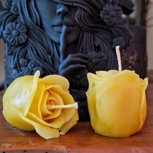 May include: Two yellow beeswax rose candles with wicks. The candles are shaped like roses and have a natural, rustic look.