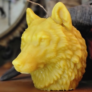 May include: A yellow beeswax candle shaped like a wolf's head. The candle has a detailed, textured surface that resembles fur.