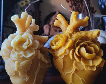 May include: Two yellow beeswax heart-shaped candles with intricate floral designs. The candles are decorated with raised flowers and leaves.
