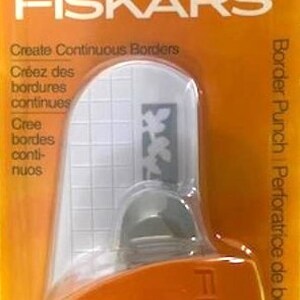 May include: Orange Fiskars border punch with a white plastic base and a leaf design. The punch is labeled "Create Continuous Borders" and "Border Punch Perforatrice de bordure | Punzón para bordes".