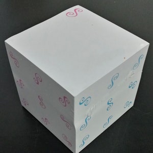 May include: A square block of white paper notes featuring a repeating pattern of small, stylized swirl symbols. The left side displays pink swirl icons, while the right side features light blue swirl icons, all printed on a stack of white paper.
