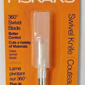 May include: A silver Fiskars 360 degree swivel knife with a clear plastic blade cover. The packaging is orange and features the text "Swivel Knife | Couteau pivotant | Cuchilla giratoria" and "Lifetime Warranty | Garantie à vie | Garantía de por vida".