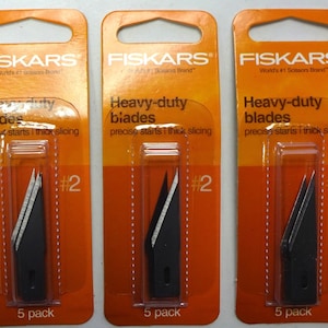 May include: Three packages of Fiskars heavy-duty blades, each containing five blades. The packages are orange and feature the Fiskars logo and the text "Heavy-duty blades" and "#2".