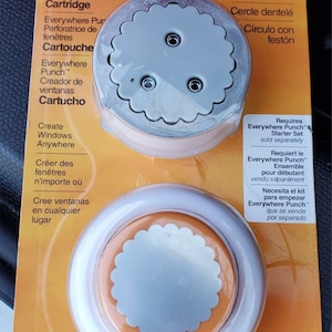 May include: A close-up of a Fiskars Everywhere Punch cartridge for creating scalloped circle window designs. The cartridge is white with a scalloped circle design and two small holes. The packaging is orange and features the text "Scalloped Circle" and "Requires Everywhere Punch Starter Set sold separately".