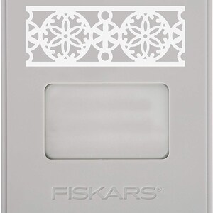 May include: Gray plastic craft punch with a white decorative border design featuring circles and floral patterns. The punch is labeled "FISKARS".
