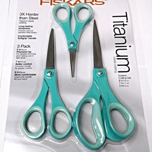 May include: A set of three Fiskars Titanium scissors in a plastic package. The scissors are turquoise blue with silver blades. The package includes a 5-inch, 7-inch, and 8-inch pair of scissors. The package says "3X Harder than Steel" and "Titanium blade coating".
