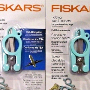 May include: Two pairs of blue folding travel scissors with TSA compliant labels. The scissors have a silver blade and a blue handle. The packaging includes the text "FISKARS" and "TSA Compliant".