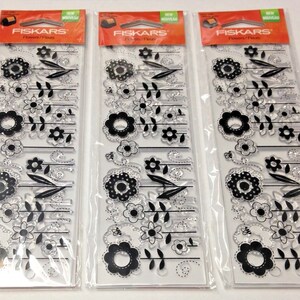 May include: Three clear plastic sheets with black floral designs. The sheets are packaged in individual plastic bags with the brand name "Fiskars" and the words "Flower Flourish" printed on the front.