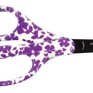 May include: A pair of Fiskars Non-Stick scissors with white and purple floral pattern handles. The blades are black, and the scissors are designed for general use. The text "FISKARS" and "NON-STICK" are printed on the blade.