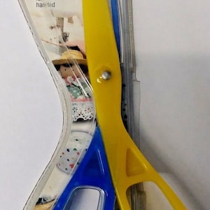 May include: A yellow and blue plastic sewing scissors with rounded tips for safety. The packaging says "SINGER My First Sewing Scissors" and "right or left handed". The item number is 00332.