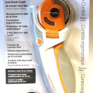 May include: White and orange Fiskars rotary cutter with a black blade. The cutter has an ergonomic design and an auto blade guard. It includes two extra 45 mm blades. Lifetime warranty.