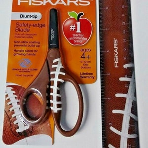 May include: A package of Fiskars safety-edge scissors with a football design. The scissors are 5 inches long and are recommended for ages 4 and up. The package also includes the text "World's #1 Scissors Brand" and "#1 teacher recommended brand!"