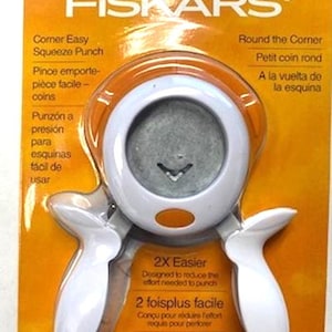 May include: White corner rounder punch with orange accents. The packaging features the Fiskars logo and the text "Corner Easy Squeeze Punch" and "Round the Corner".