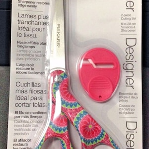 May include: A pink and blue patterned pair of 8-inch scissors with a matching pink and white sharpener. The packaging includes the text "Designer" and "Full Lifetime Warranty".