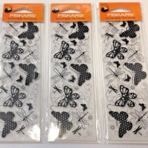 May include: Three clear plastic sheets with black and white butterfly and dragonfly designs. The sheets are packaged in clear plastic and labeled "FISKARS Summer Wings/Ailes estivales".