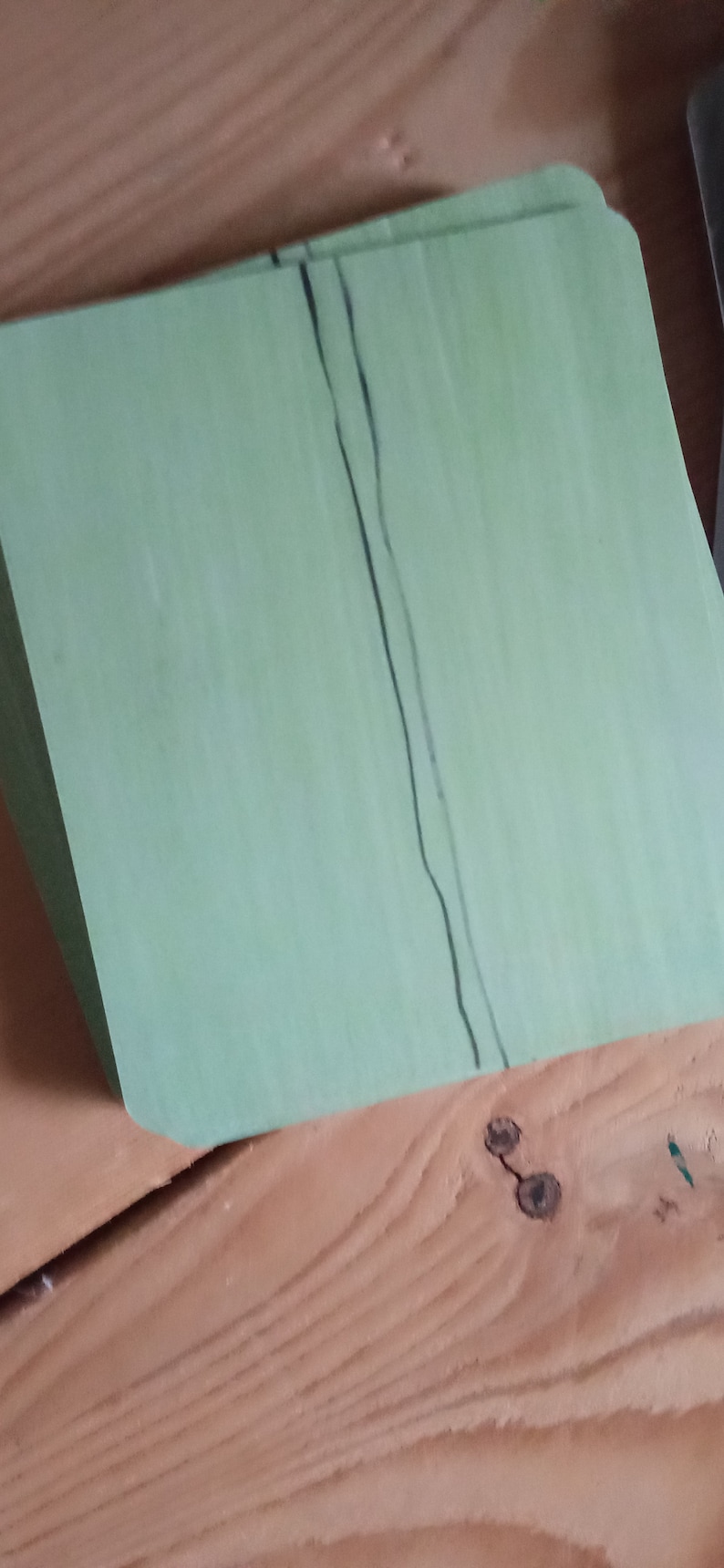 May include: A stack of light green paper sheets with a black line running down the center.