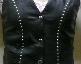 May include: A black leather vest with silver studs and a button closure. The vest has a pointed hem and two pockets.