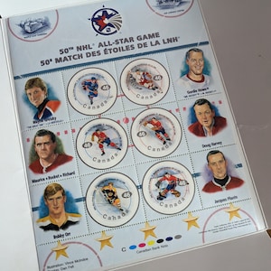 Puede incluir: Un conjunto de nueve sellos canadienses con jugadores de hockey del 50º Juego de Estrellas de la NHL. Los sellos son circulares y muestran a los jugadores con sus uniformes de hockey. Los sellos son todos rojos, blancos y azules con las palabras "Canadá" y "46" impresas en ellos.