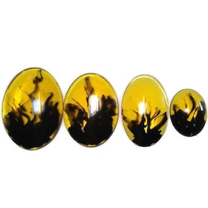 May include: Four oval-shaped resin cabochons with black ink swirls inside. The cabochons are different sizes and are arranged in a row from largest to smallest.