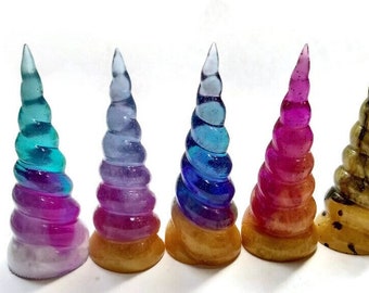 Peut inclure: Cinq figurines de corne de licorne colorées avec un design en spirale. Les cornes sont en résine et ont une finition brillante. Les cornes sont montées sur des bases en bois.